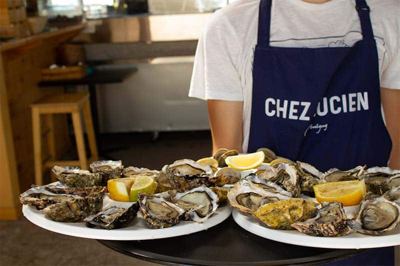 Serveur de chez Lucien portant des assiettes d'huîtres.